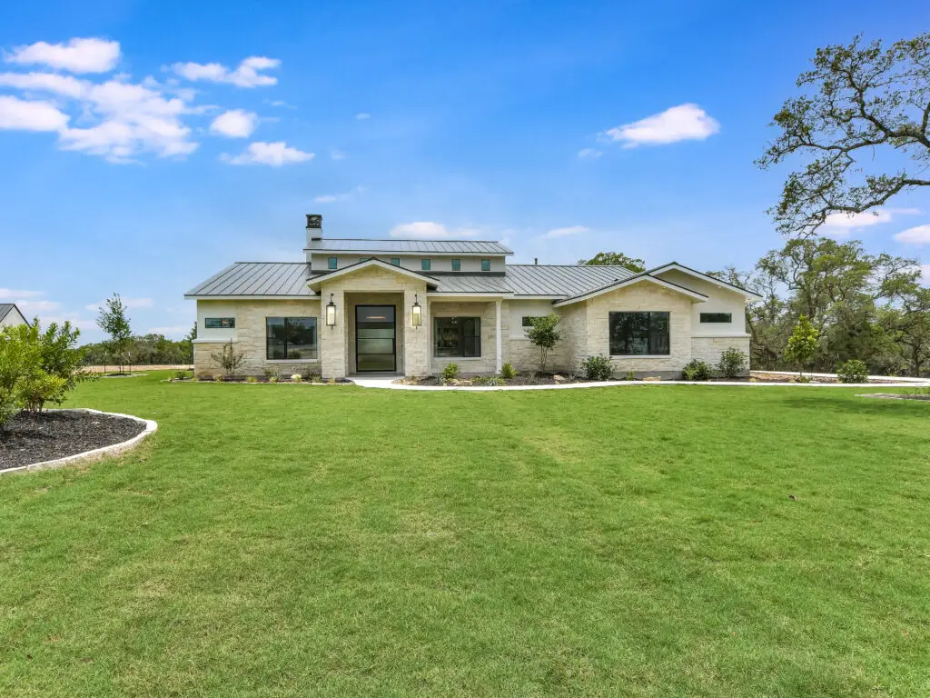Single-story stone home with metal roof, modern entry, and expansive manicured lawn