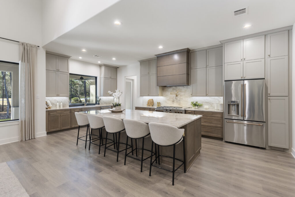 Kitchen with large island in Design Tech Homes showcase model at the Estates of Texas Grand Ranch featuring custom cabinetry and open layout