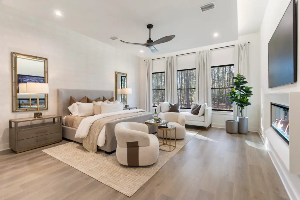 Bright, modern bedroom with a neutral color palette, upholstered bed, seating area, and large windows with French doors leading outside.